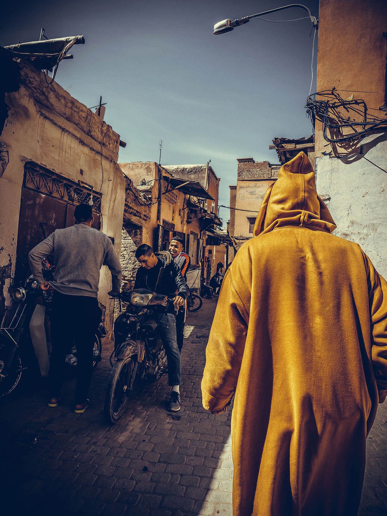 A figure in a mustard-yellow hooded robe walks down a busy street