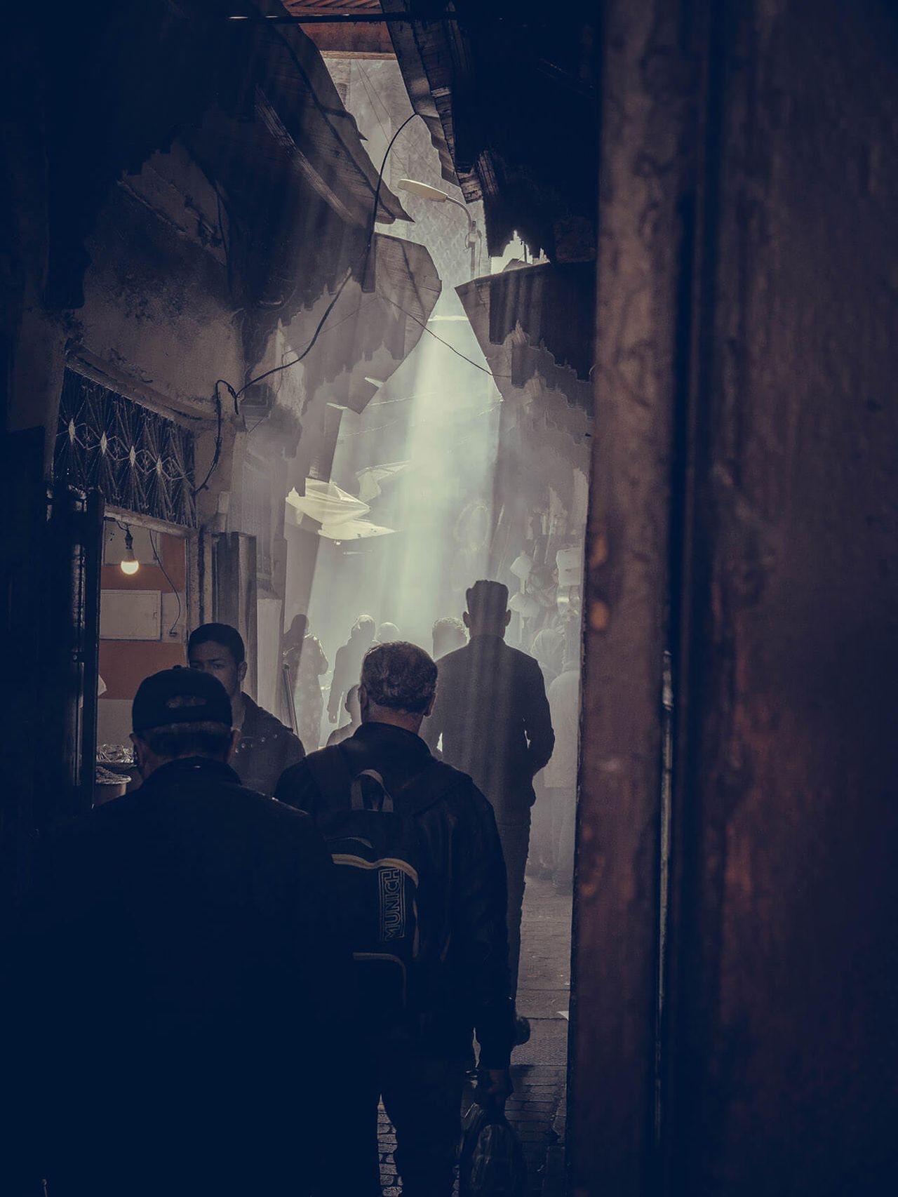Silhouetted people walk through a smoky, shadowed passageway