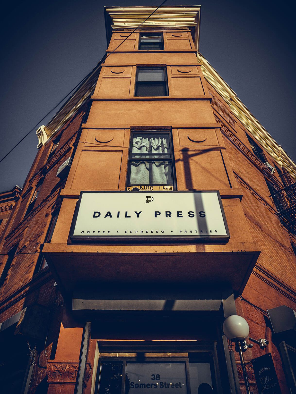 Looking up at the sign of a narrow brick corner building against a dusk sky