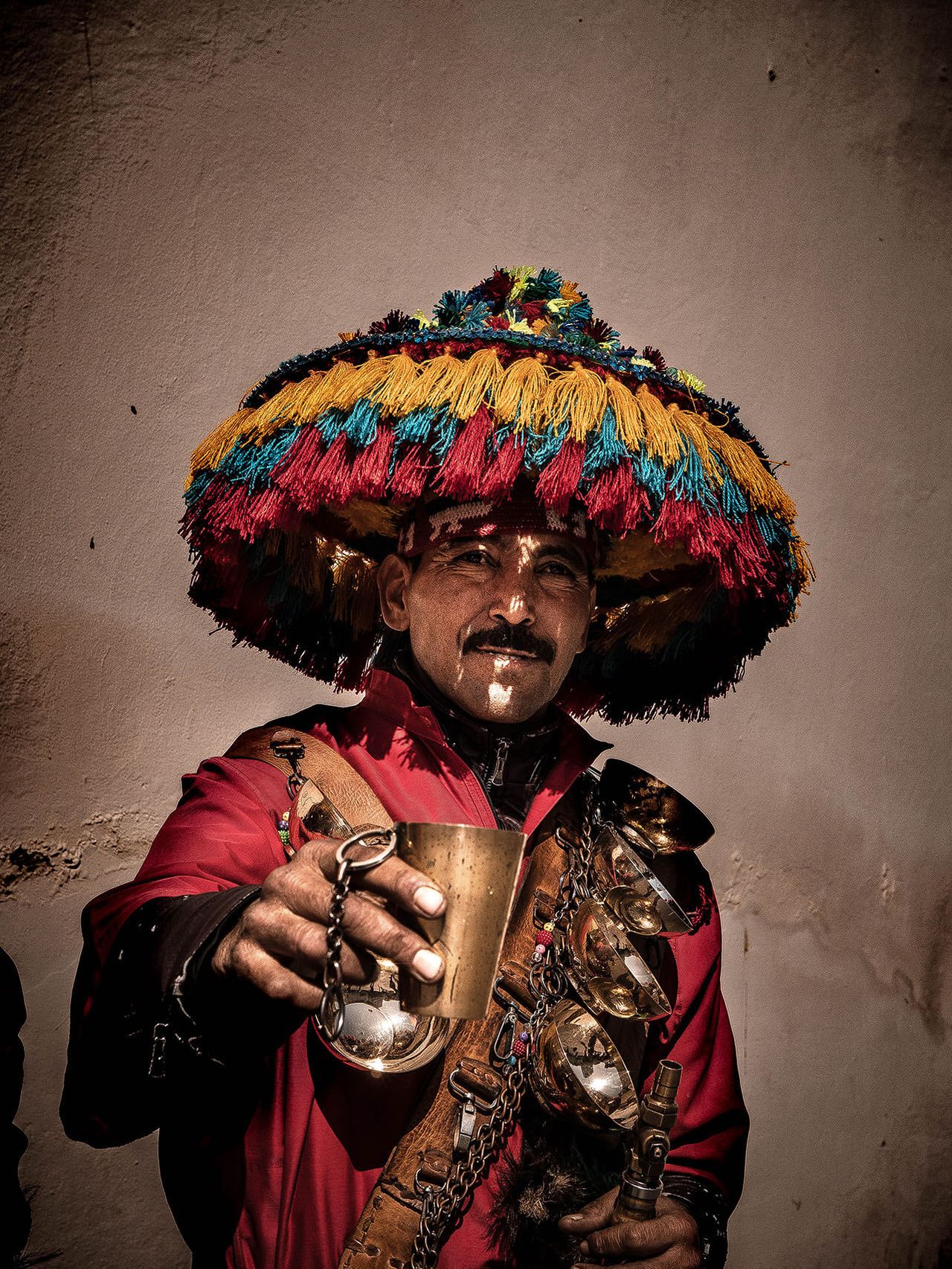 A water seller in a colorful fringed hat holds out a brass cup