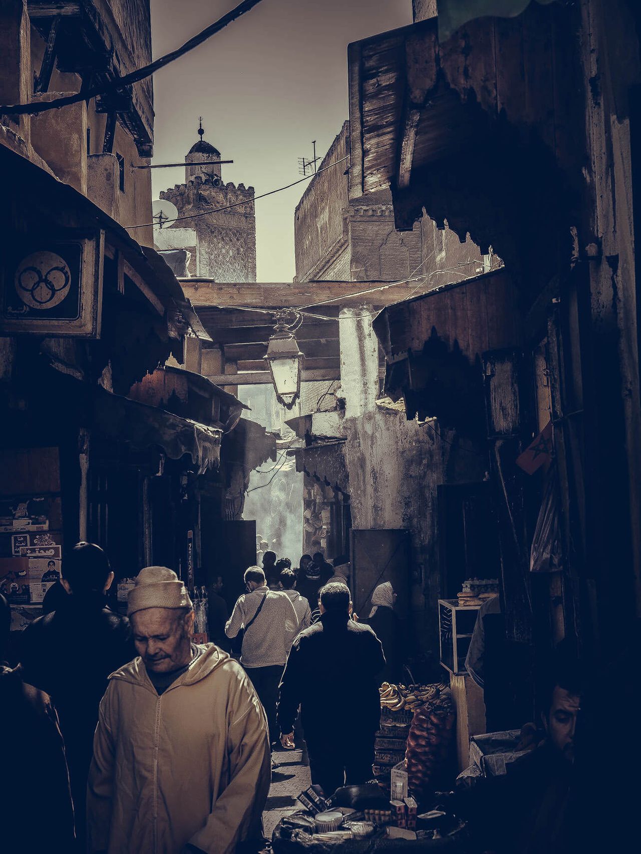 A crowded market street lined with awnings, a minaret in the distance