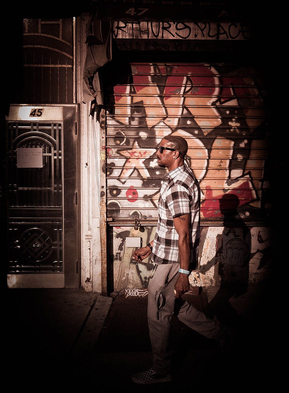 A man walks past a graffiti-covered roll-up door at night