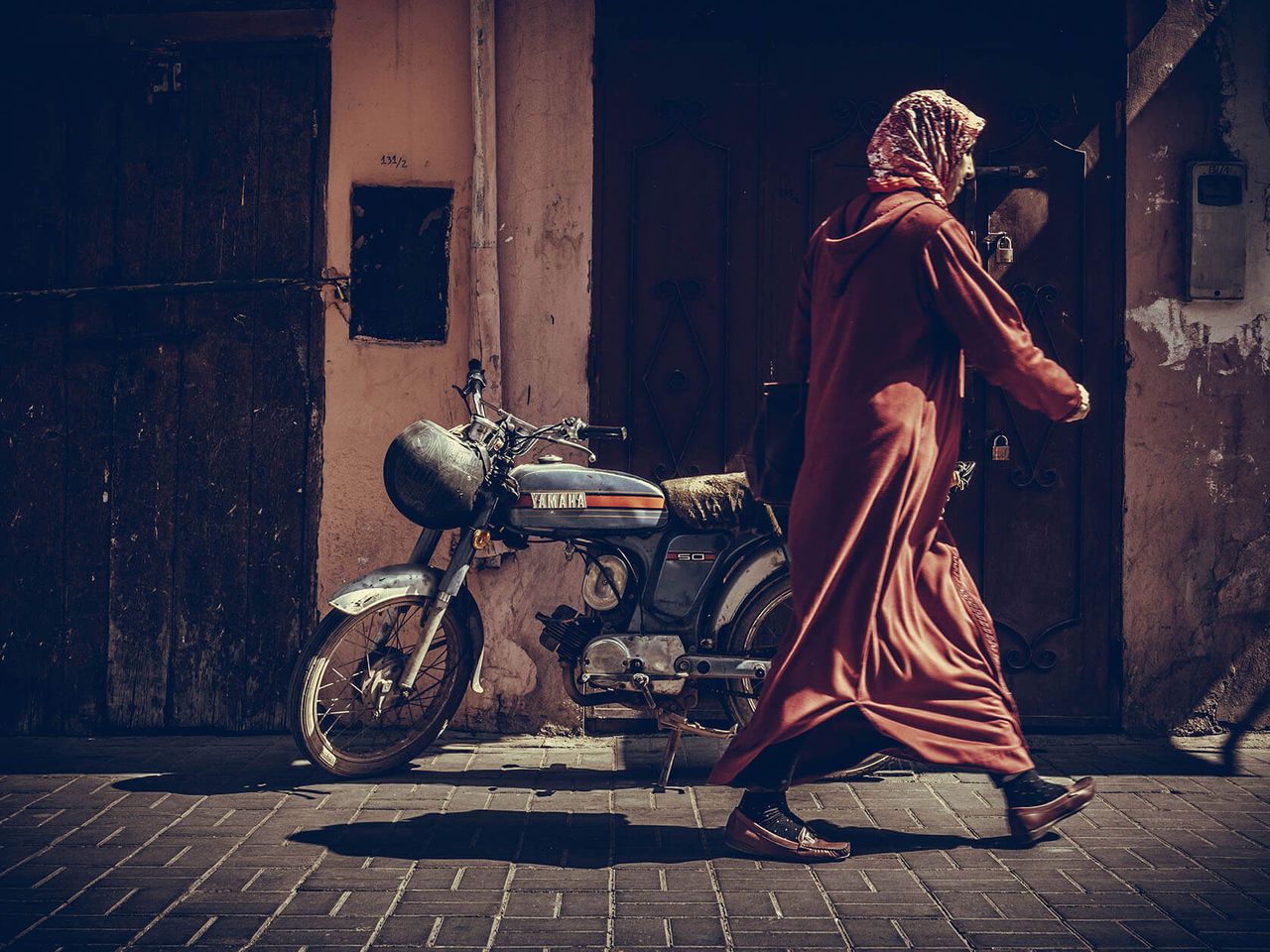 A woman in a red robe walks past a parked motorbike