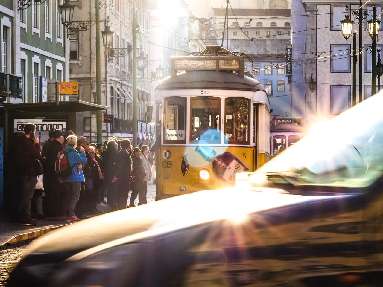 A yellow streetcar and a crowd of riders in a burst of sun flare